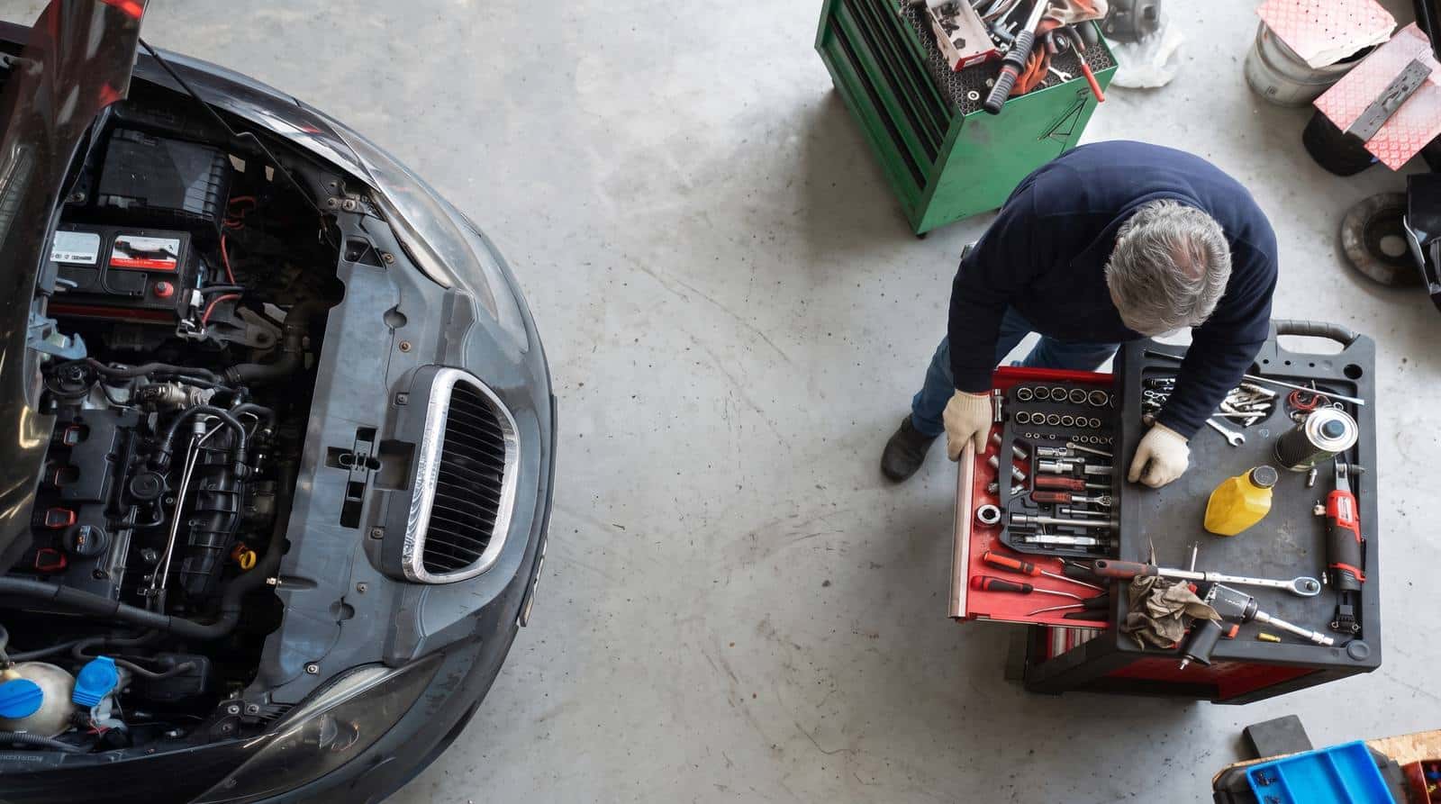 Vista cenital de un mecánico con guantes revisando el motor de un auto